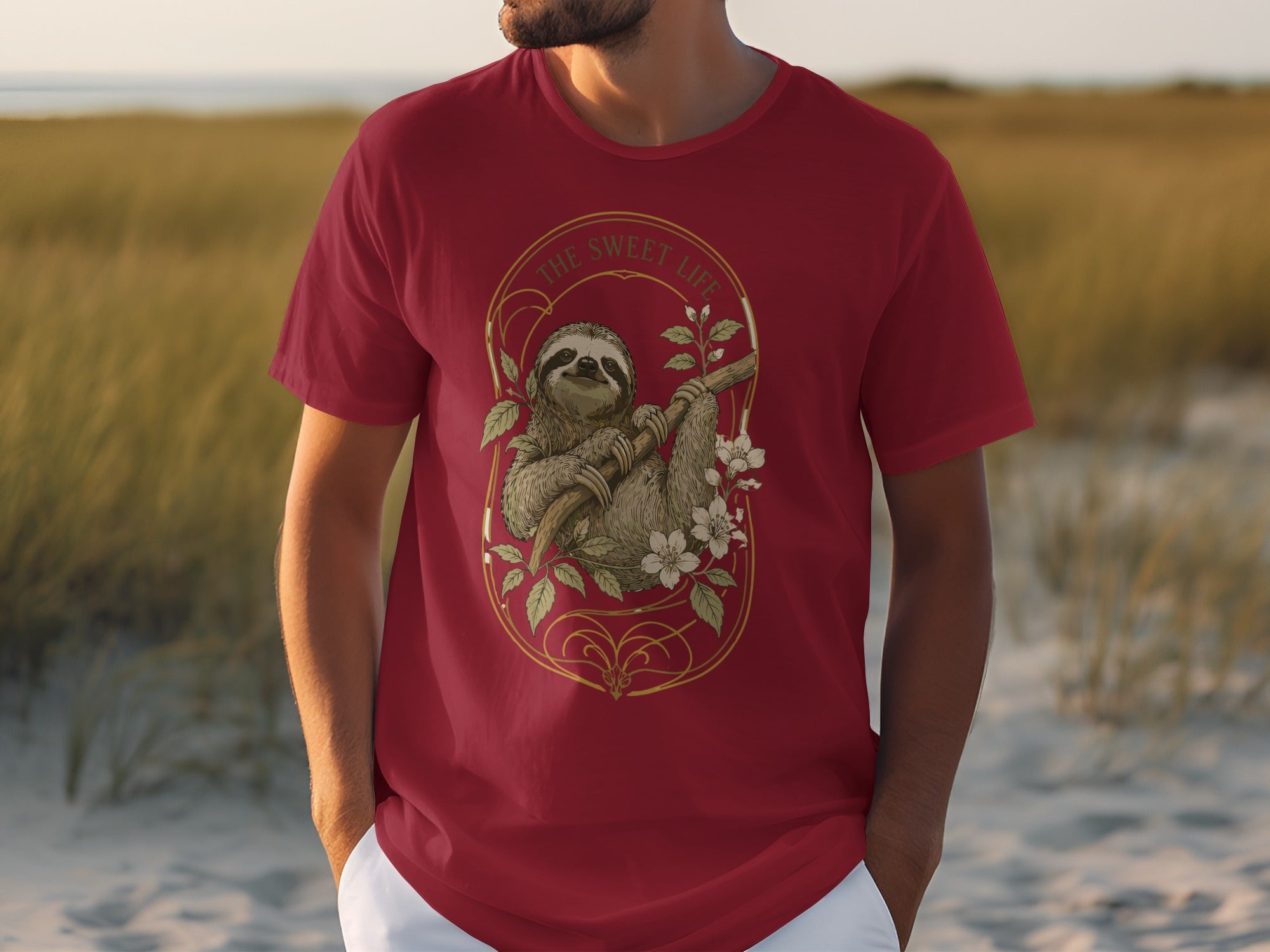 Red t-shirt with a golden oval design featuring a sloth on a branch with flowers.